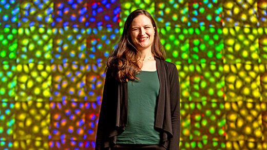 Photo of Anne Carpenter of the Broad Institute standing in front of a wall of colored microscopy images.