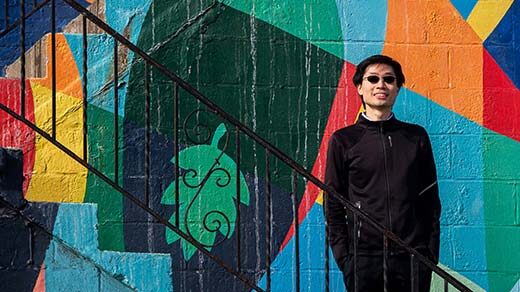 Po-Shen Loh standing on a stairway in front of a colored wall outside of his office in Pittsburgh.