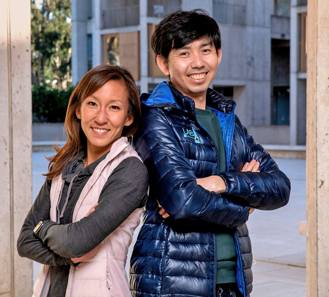 Profile photo of researchers Kay Tye and Hao Li of the Salk Institute for Biological Studies smiling and standing back-to-back.